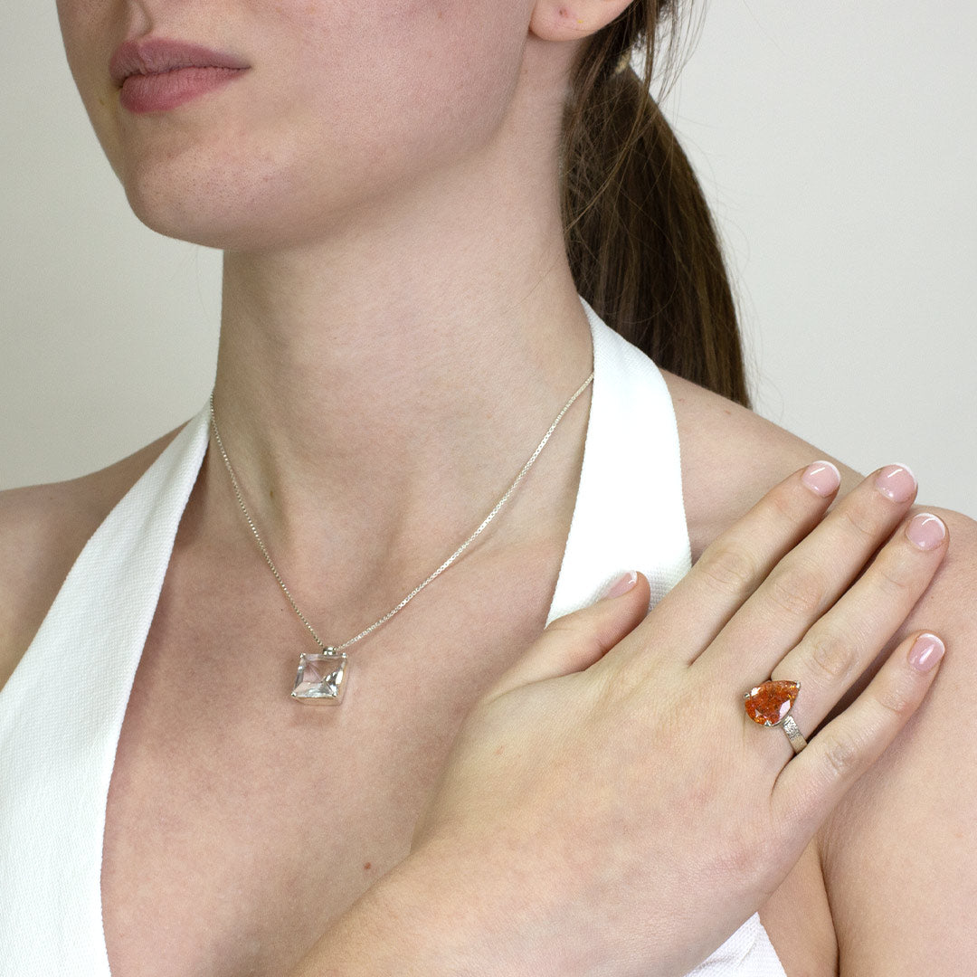 Woman wearing a silver ring with a teardrop-shaped orange gemstone on a white background