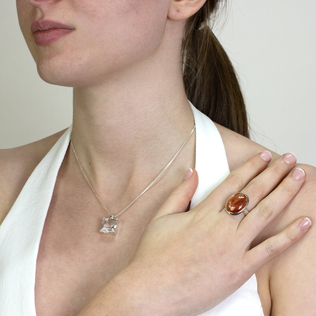 Woman wearing a silver ring with an oval orange gemstone on a plain background