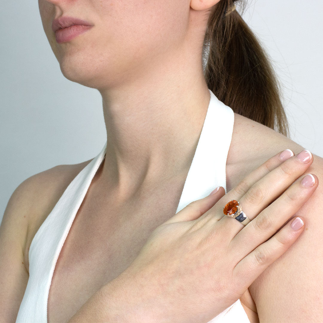 Woman wearing a silver ring with an orange gemstone on a plain background