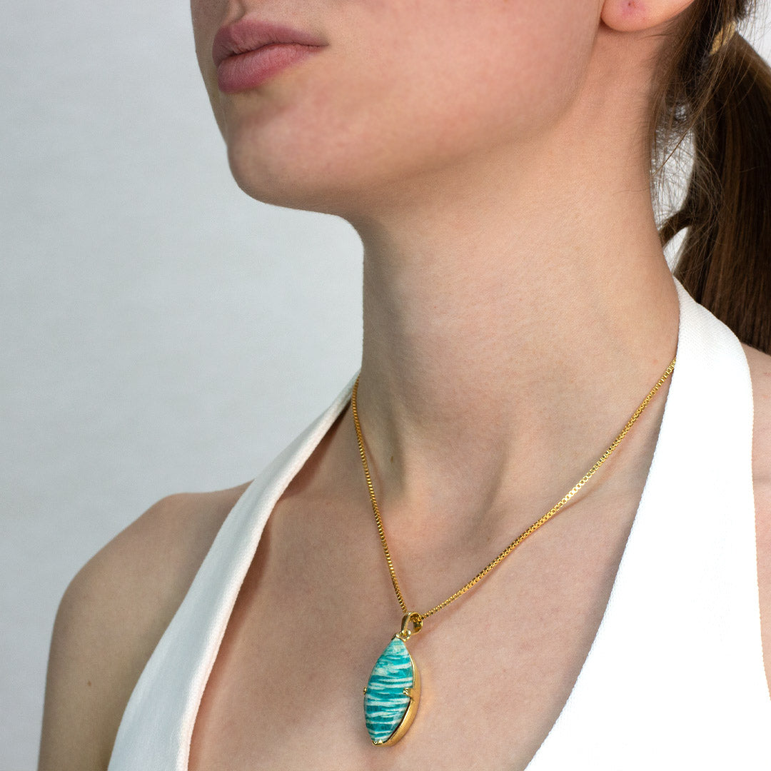 Woman wearing a golden necklace with a green pendant on a plain background