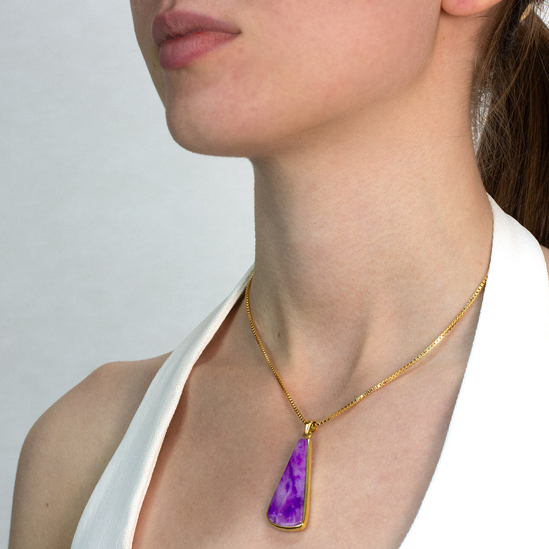 Woman wearing a golden necklace with a purple pendant against a neutral background