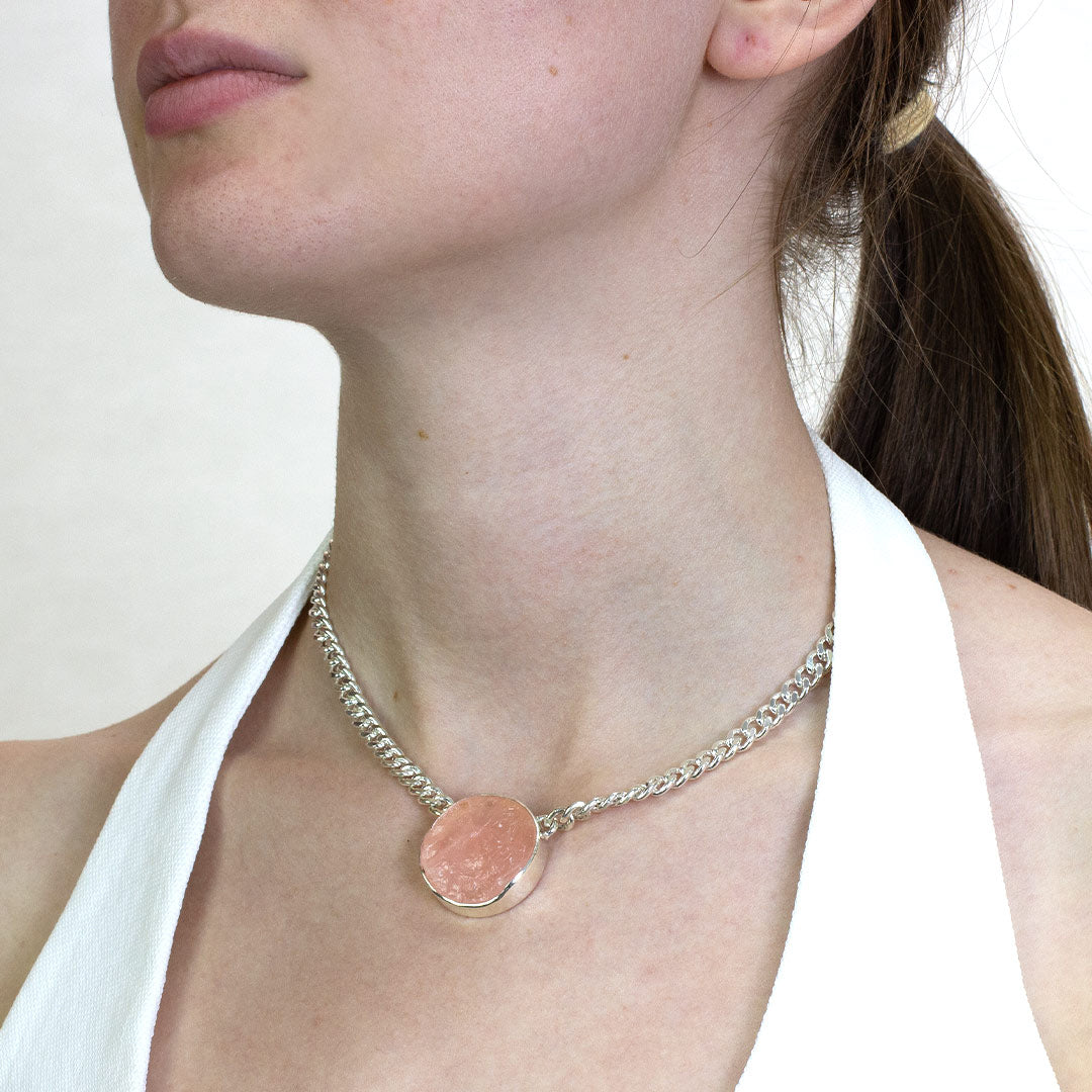 Woman wearing a silver necklace with a pink raw gemstone on a plain background