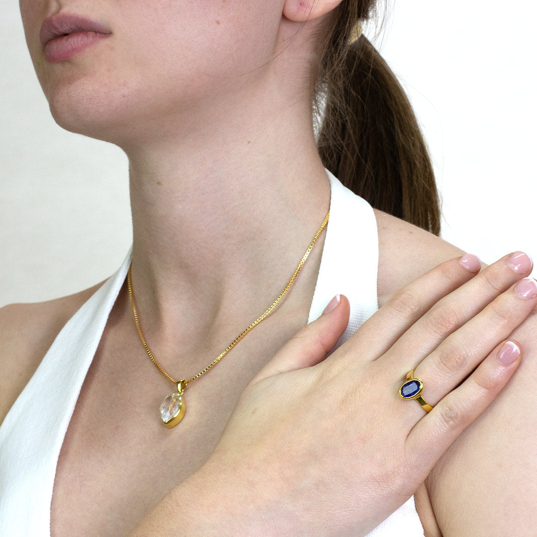 Woman wearing a gold ring with a blue gemstone on a plain background