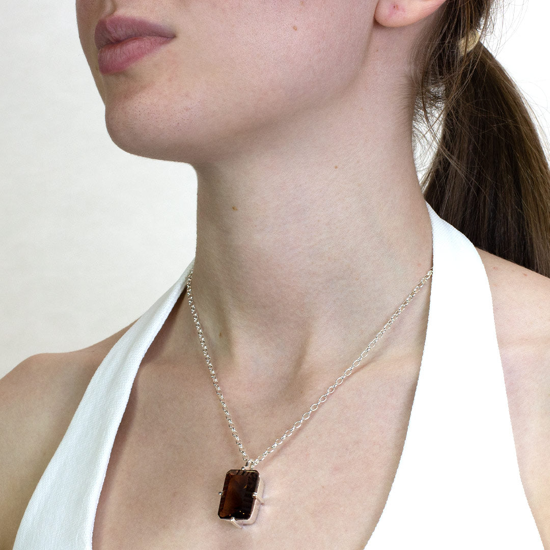 Woman wearing a silver necklace with a rectangular smoky gemstone on a plain background