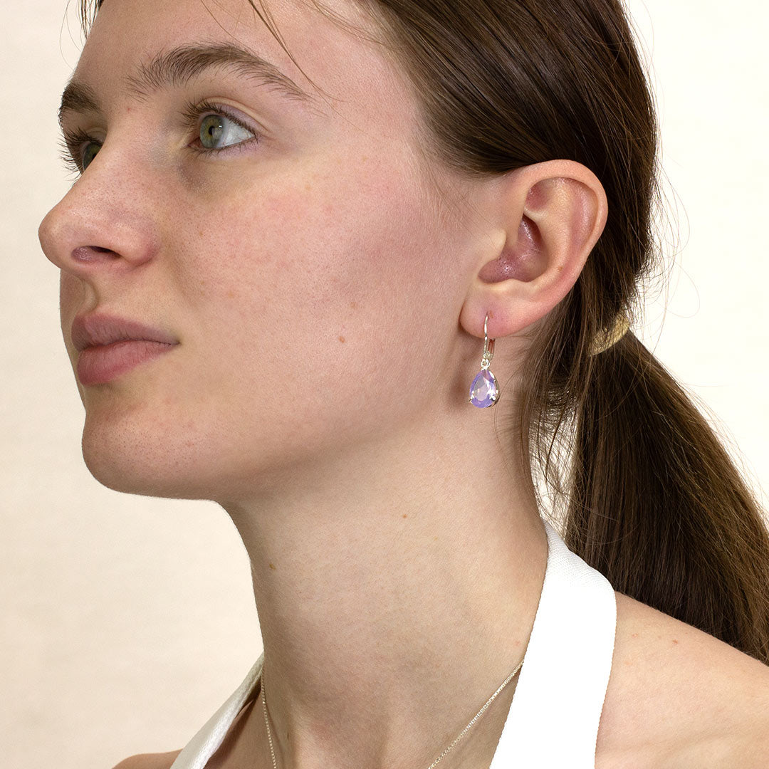 Close-up of a woman wearing a purple teardrop earring on a plain background