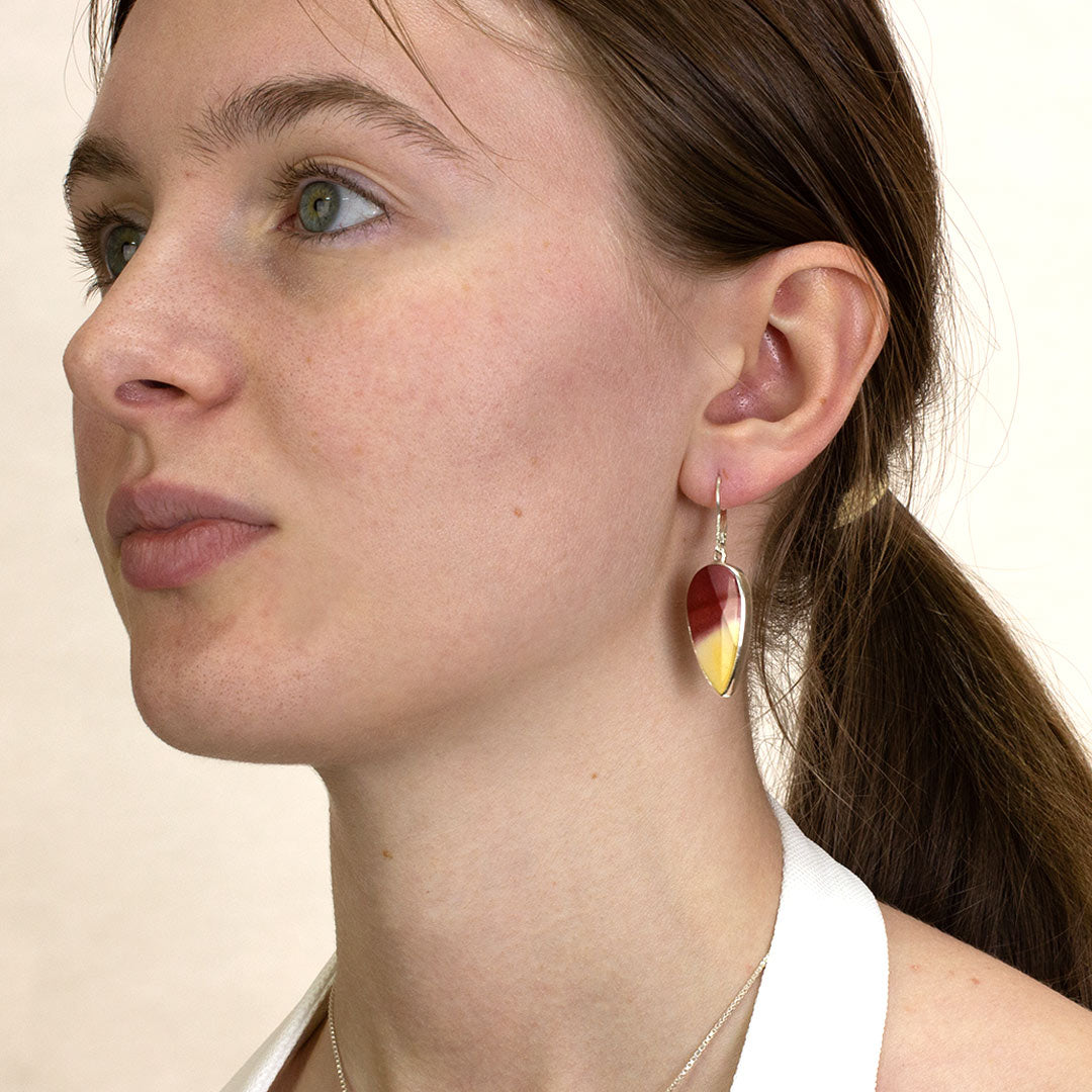 Close-up of a woman wearing a silver drop earring with red and yellow gemstone on a plain background