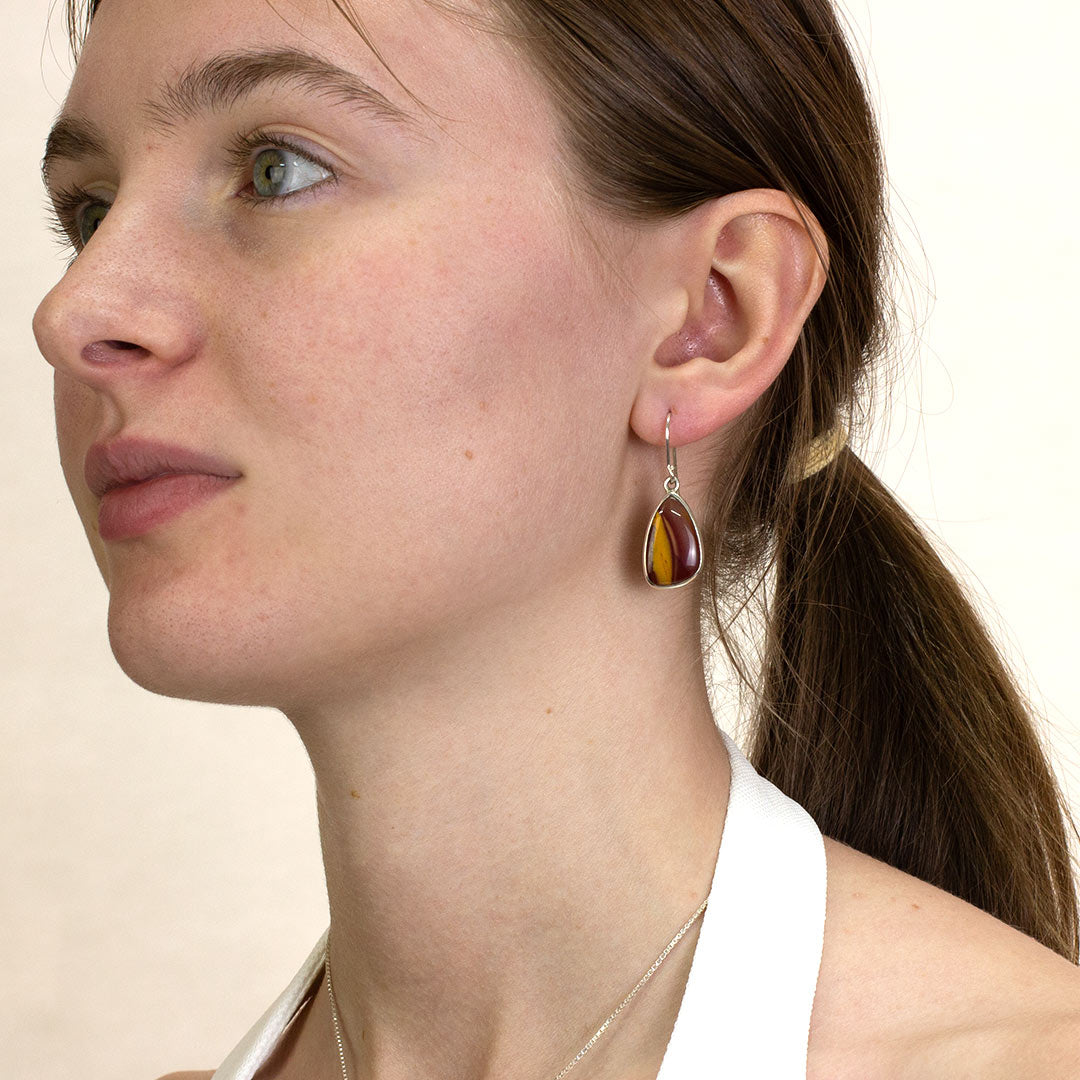 Close-up of a woman wearing a silver drop earring with red and yellow gemstone on a plain background