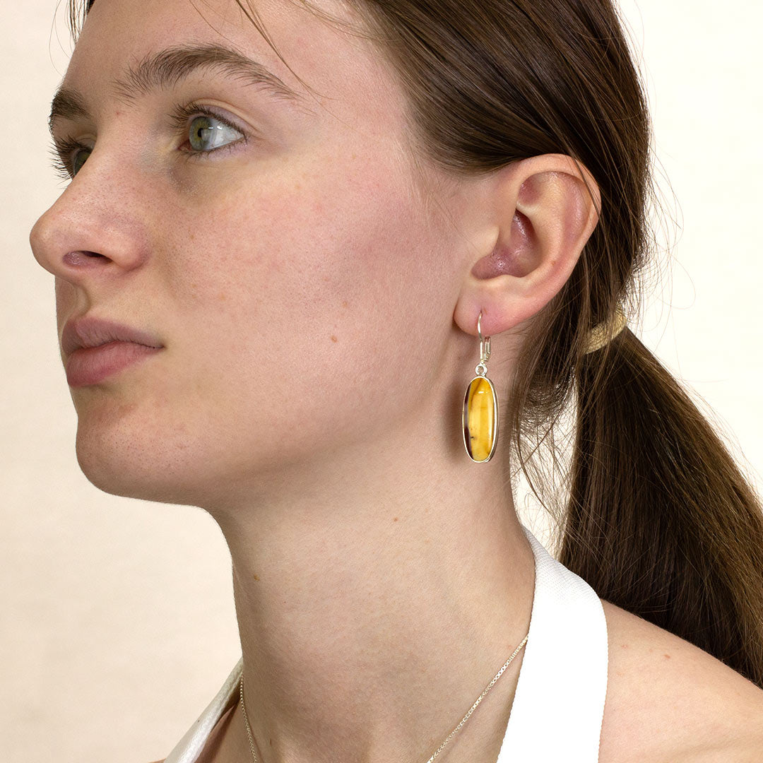 Close-up of a woman wearing a silver drop earring with red and yellow gemstone on a plain background