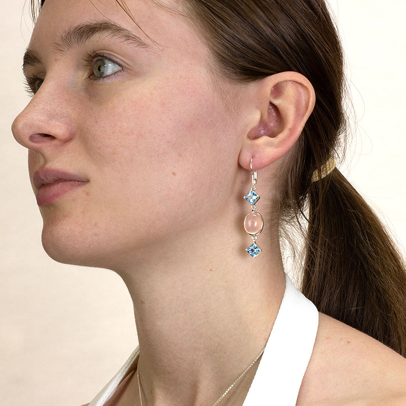 Close-up of a woman wearing a silver drop earring with pink and blue gemstones on a white background