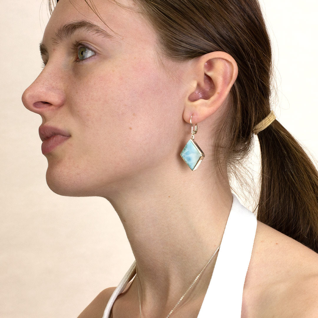 Close-up of a woman wearing a silver drop earring with blue and white gemstone on a plain background