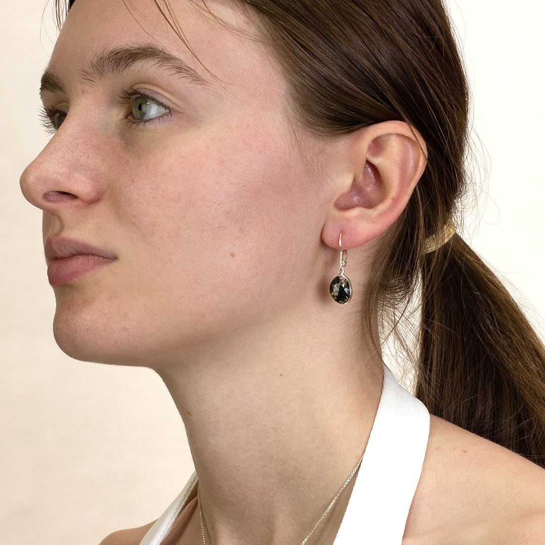 Close-up of a woman wearing a silver drop earring with translucent stone with dark green inclusions on a plain background