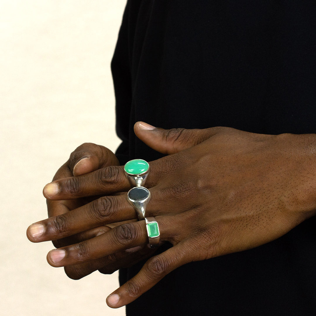 Close-up of a person's hands wearing a silver ring with a green gemstone on a plain background