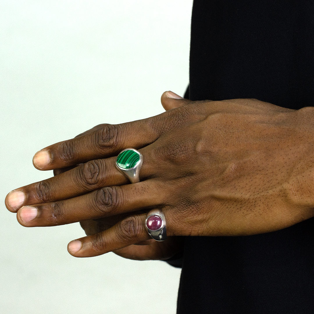 Hand wearing a silver ring with a red gemstone on a plain background