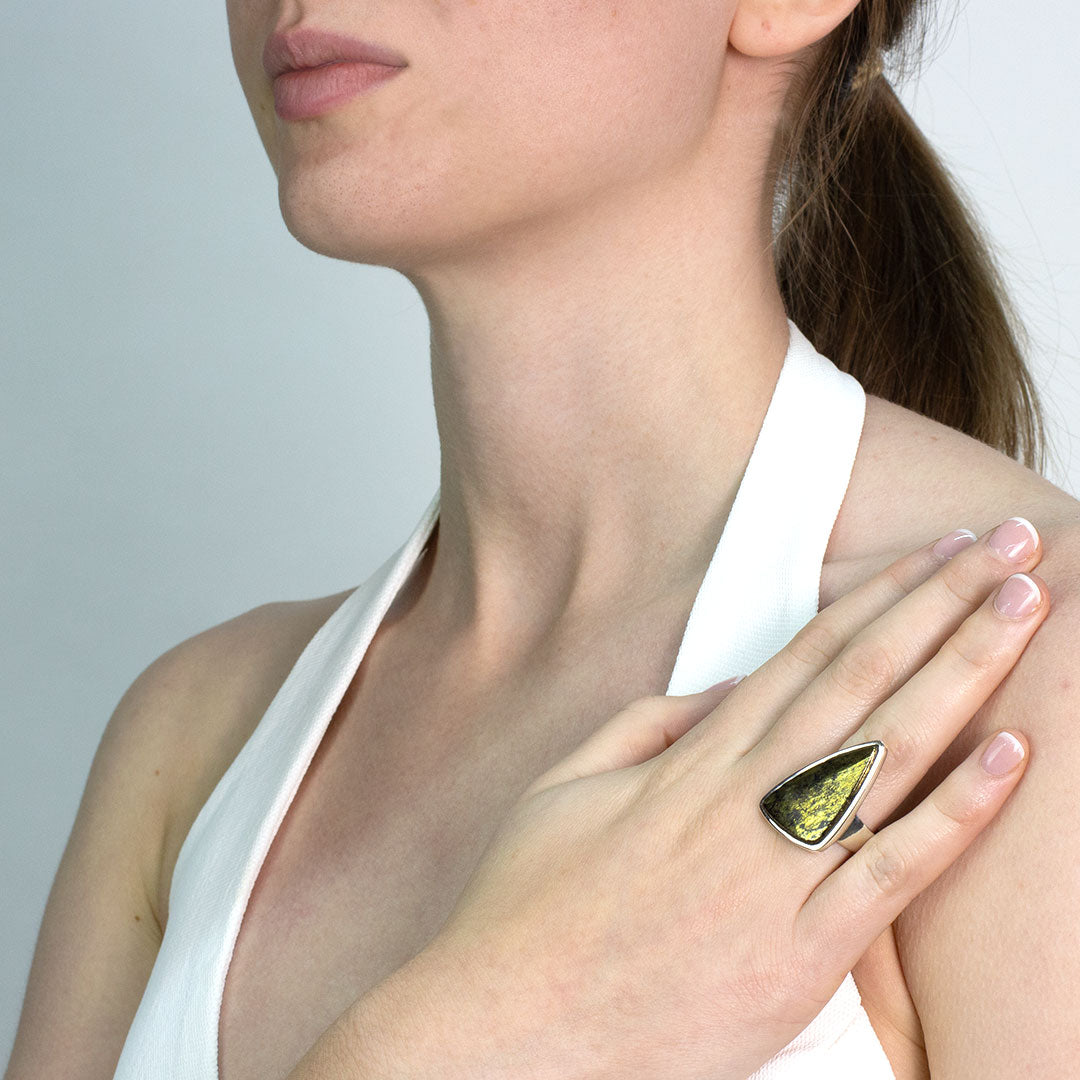 Woman wearing a silver ring with a metallic stone on a plain background