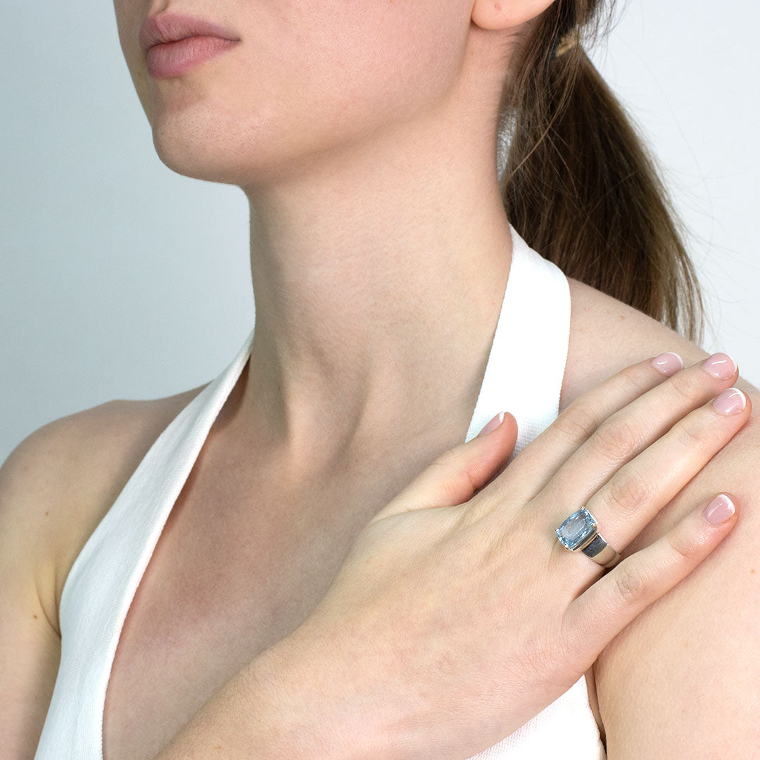 Woman wearing a silver ring with a blue gemstone on a plain background