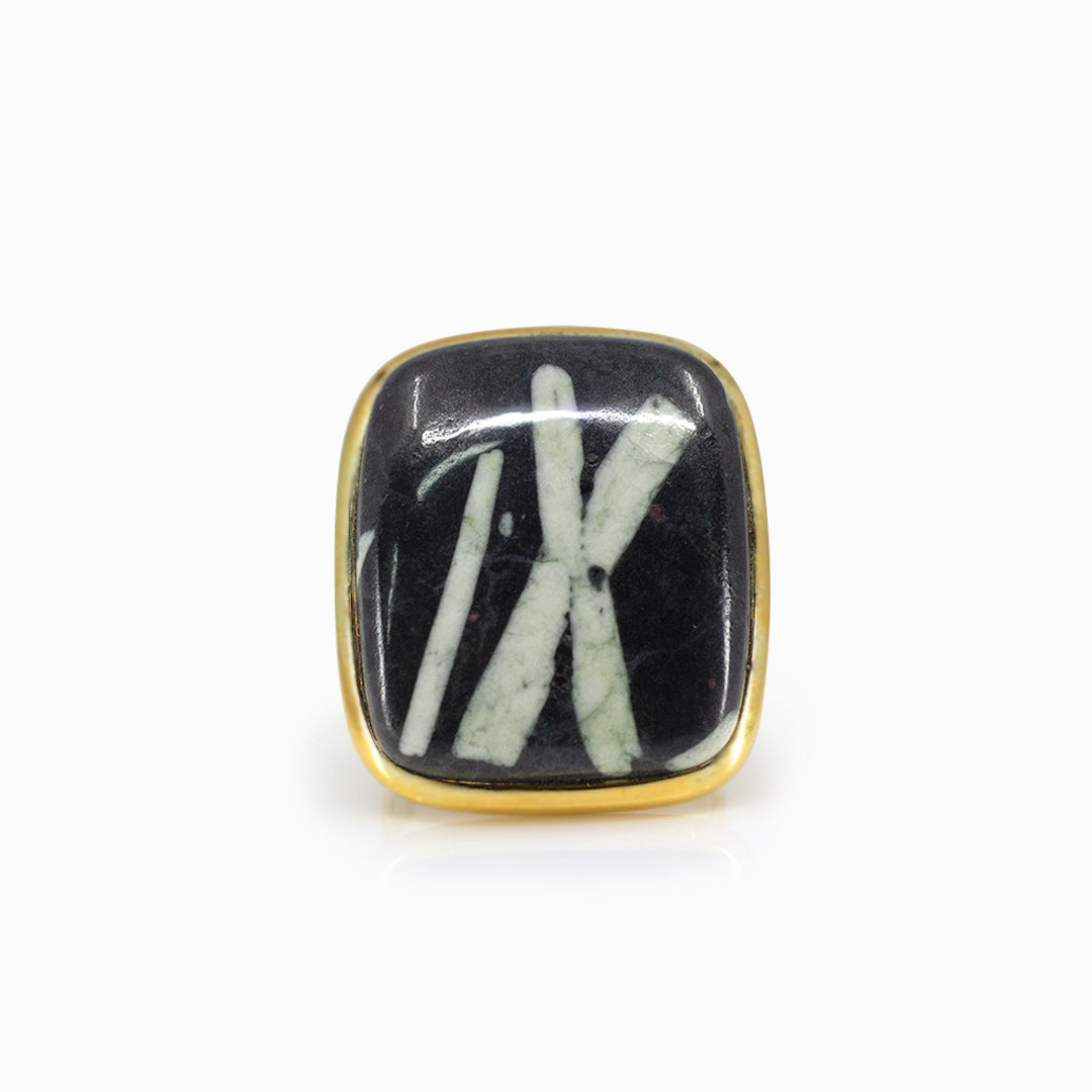 Golden ring with a black rectangular stone with white lines on a white background