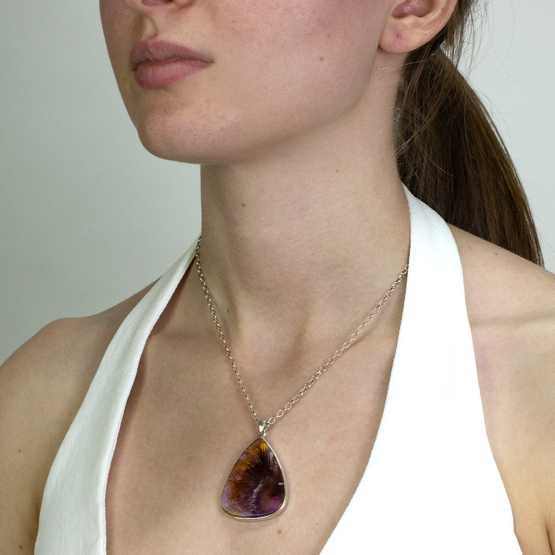 Woman wearing a silver necklace with a purple and yellow gemstone on a plain background