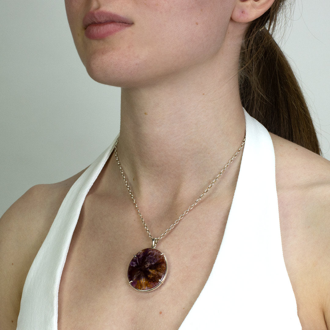 Woman wearing a necklace with a silver necklace with a purple and yellow stone on a plain background