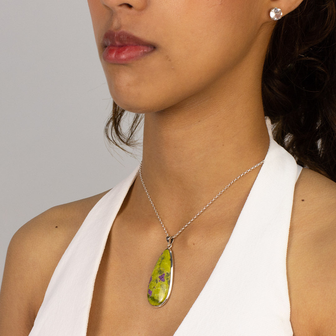 Woman wearing a silver teardrop-shaped pendant with green and purple patterns on a plain background