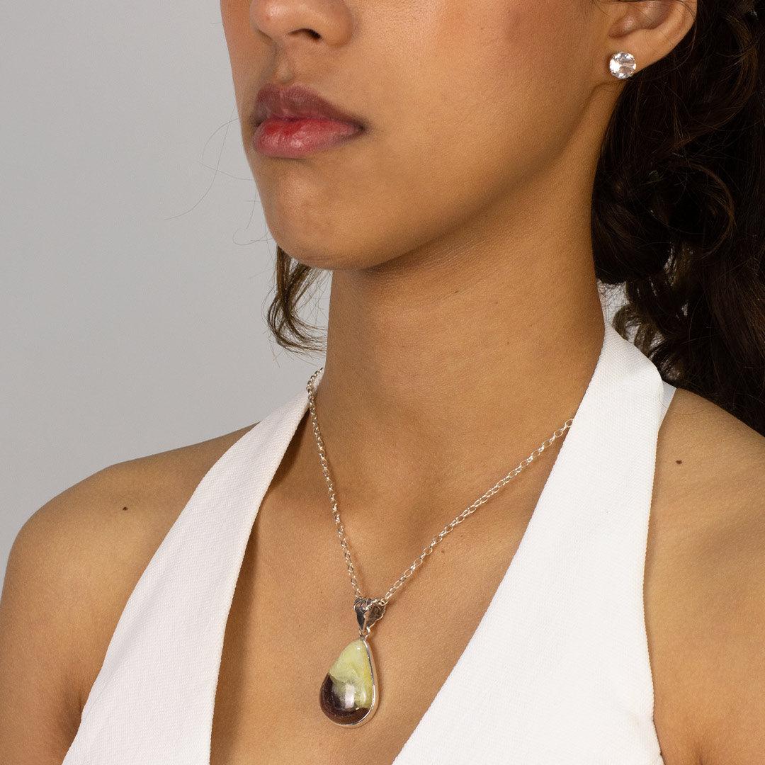 Woman wearing a necklace with a teardrop-shaped gemstone pendant on a plain background