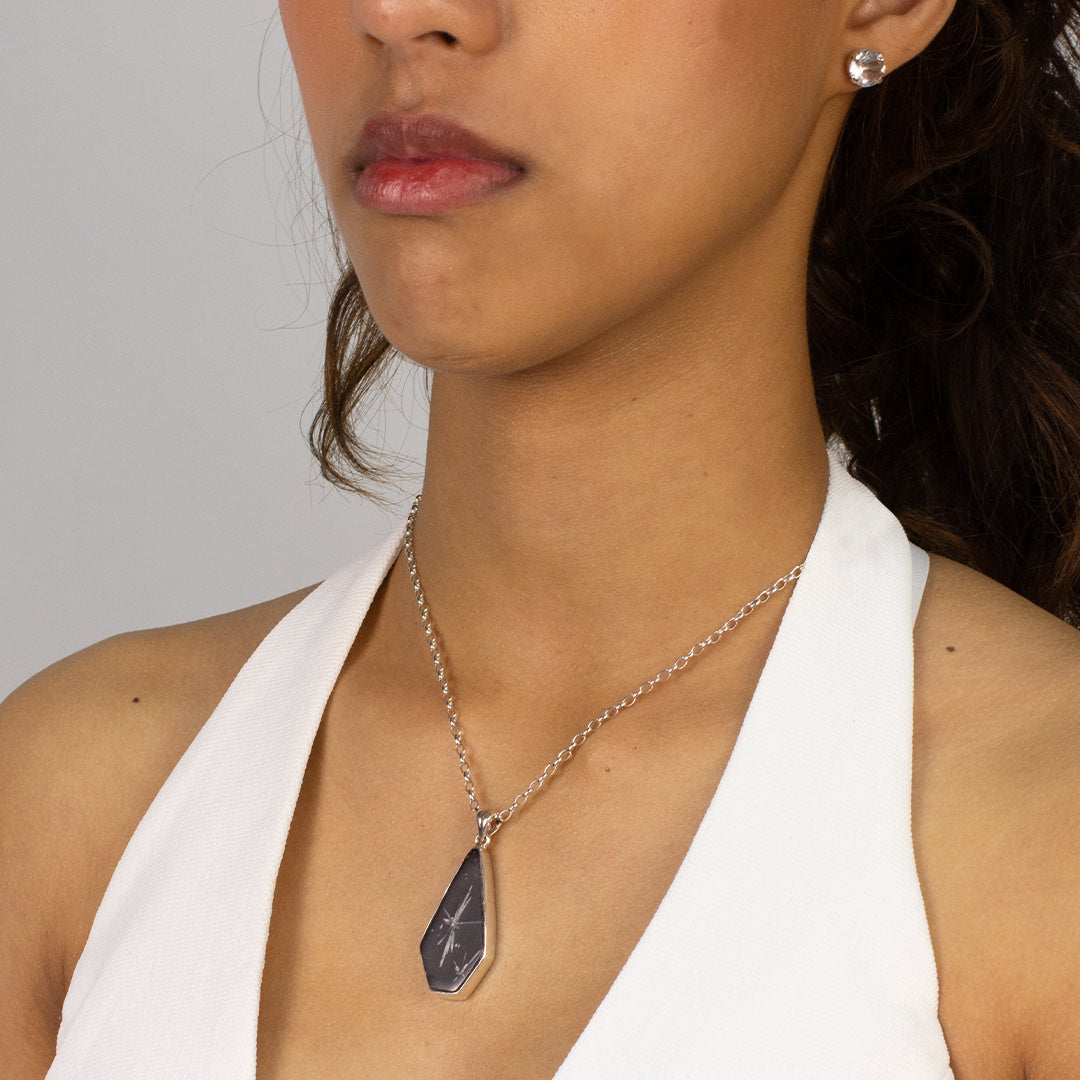 Woman wearing a black freeform pendant on a silver chain against a plain background