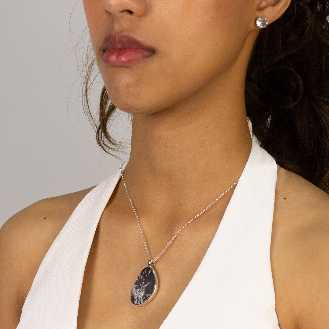 Woman wearing a silver necklace with a black freeform pendant on a plain background