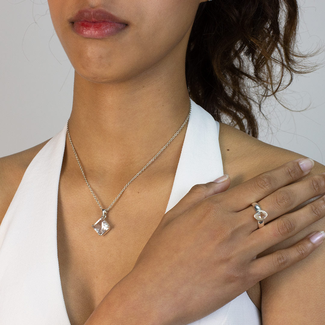 Woman wearing a silver ring with a clear gemstone on a plain background