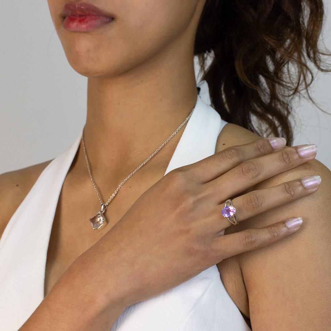 Woman wearing a silver ring with a purple gemstone on a plain background