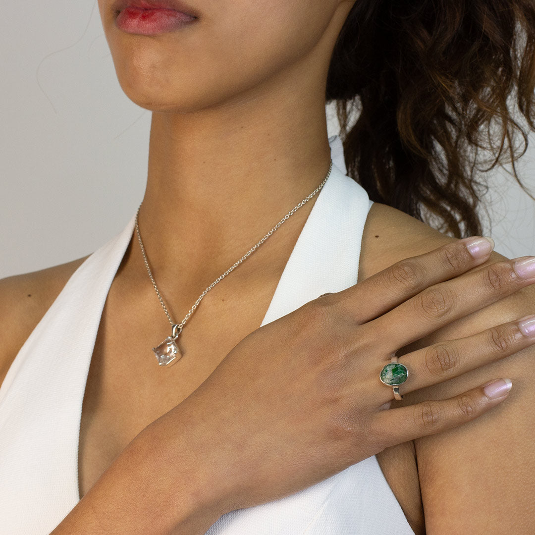 Woman wearing a silver ring with a green stone on a plain background