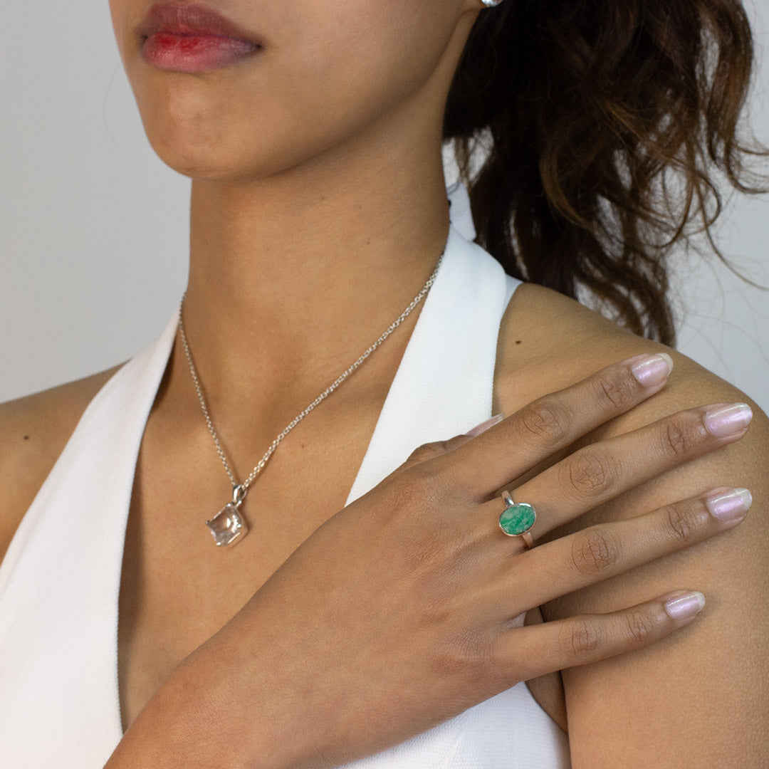 Woman wearing a silver ring with a green stone on a plain background