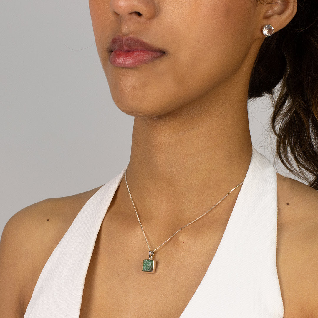Woman wearing a necklace with a green stone pendant on a plain background