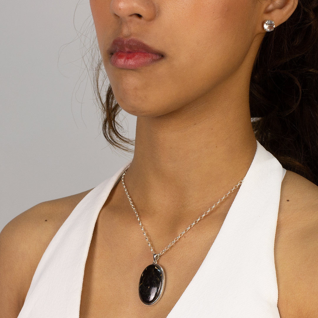 Woman wearing a necklace with a black pendant on a plain background