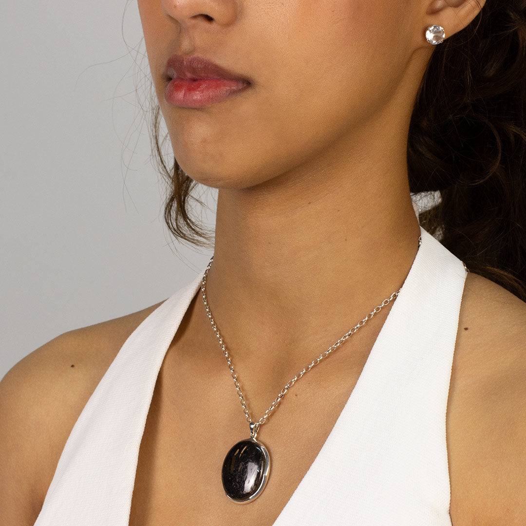 Woman wearing a silver necklace with an oval black stone pendant on a plain background