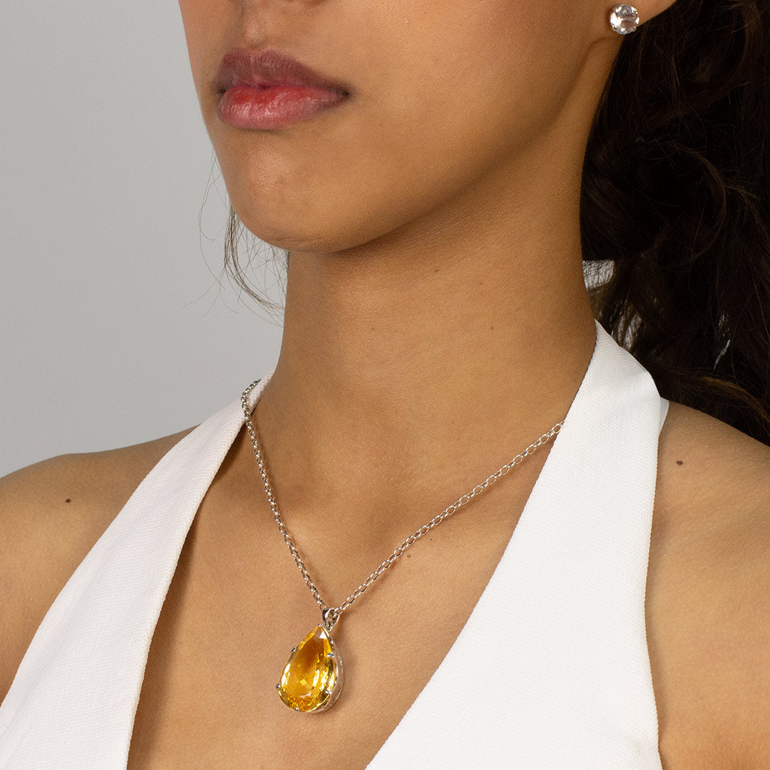 Woman wearing a teardrop-shaped yellow gemstone pendant on a plain background