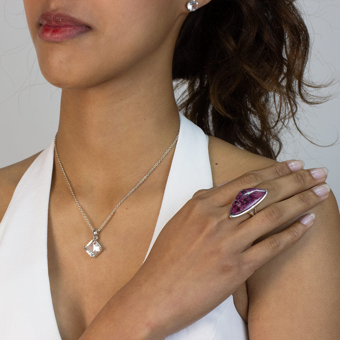 Woman wearing a silver ring with a freeform gemstone on a plain background