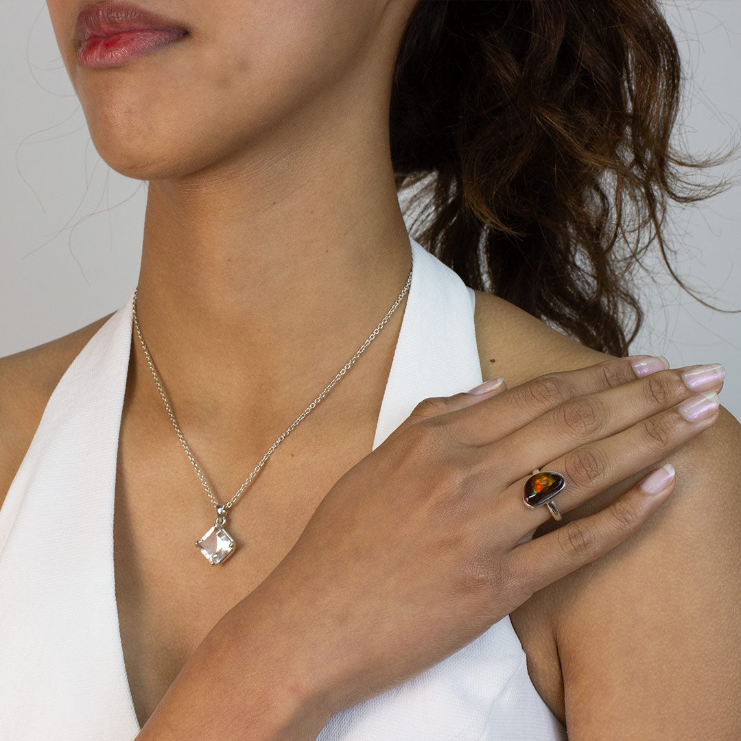 Woman wearing a silver ring with a brown and green freeform stone on a plain background