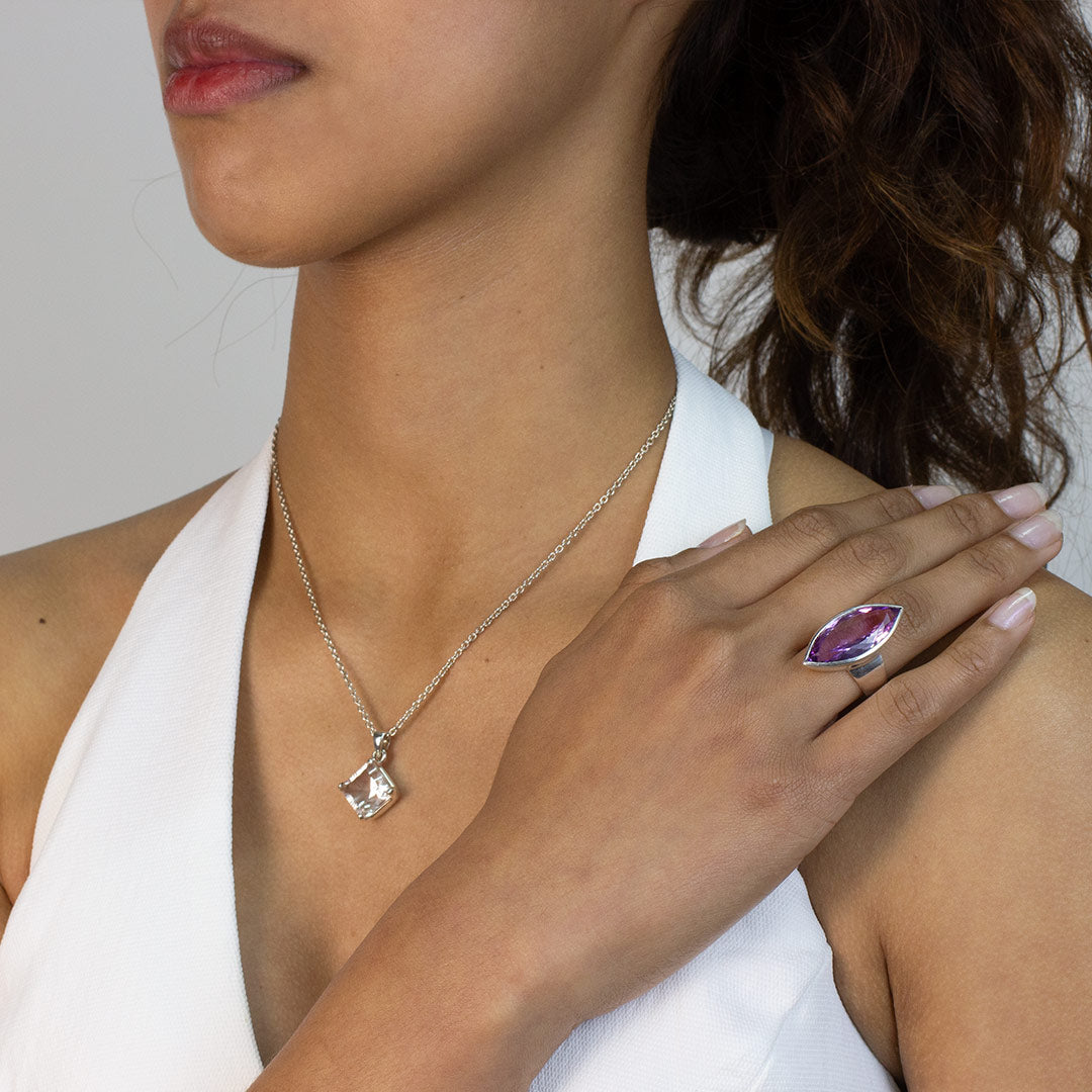 Woman wearing a silver ring with a marquise-shaped purple gemstone on a plain background