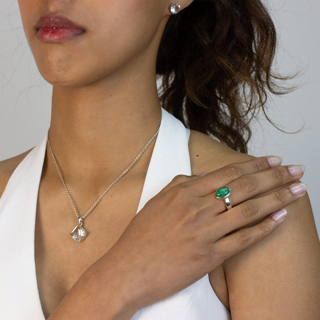 Woman wearing a silver ring with a green stone on a plain background
