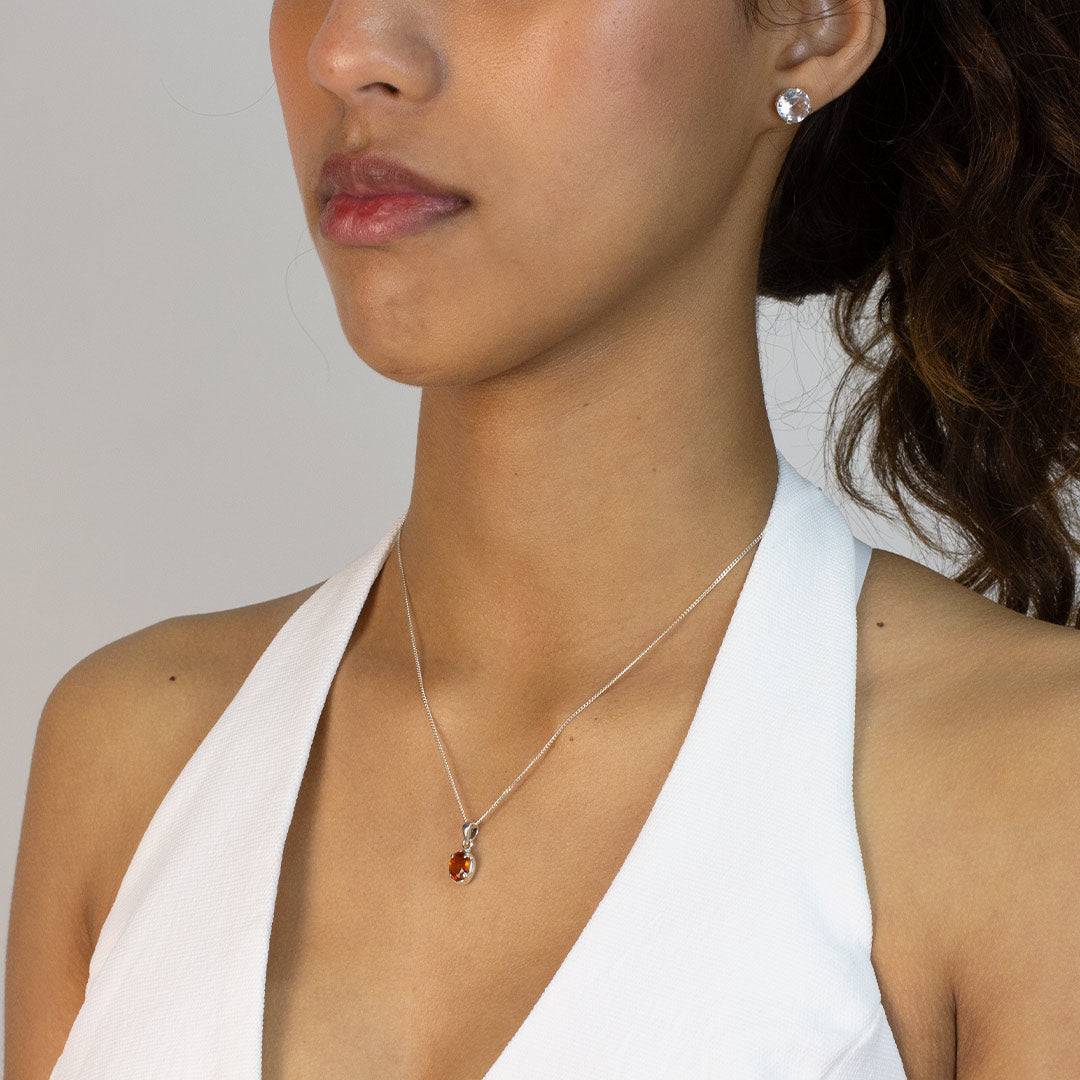 Woman wearing a necklace with a pendant featuring an orange gemstone on a plain background