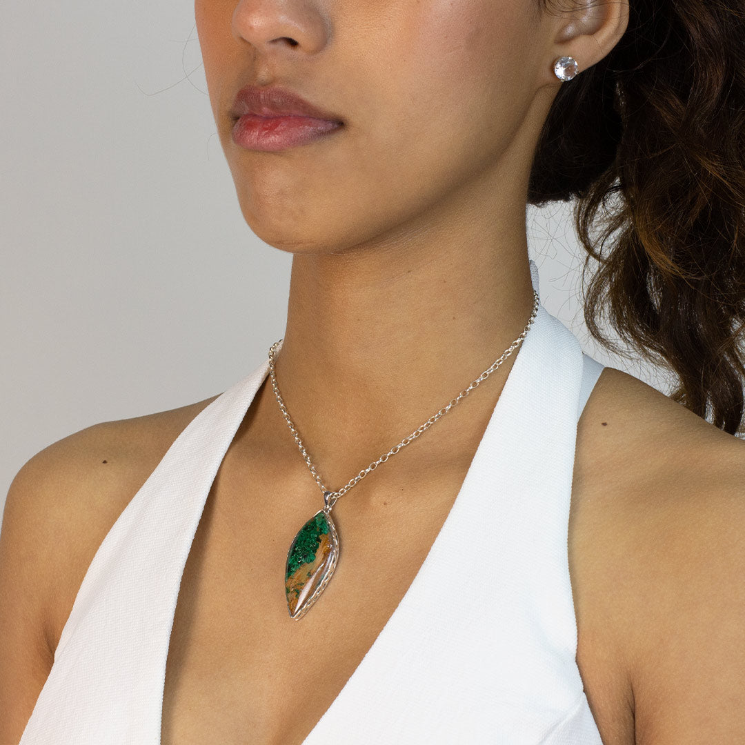 Woman wearing a silver necklace with a pendant featuring green and brown stone on a plain background
