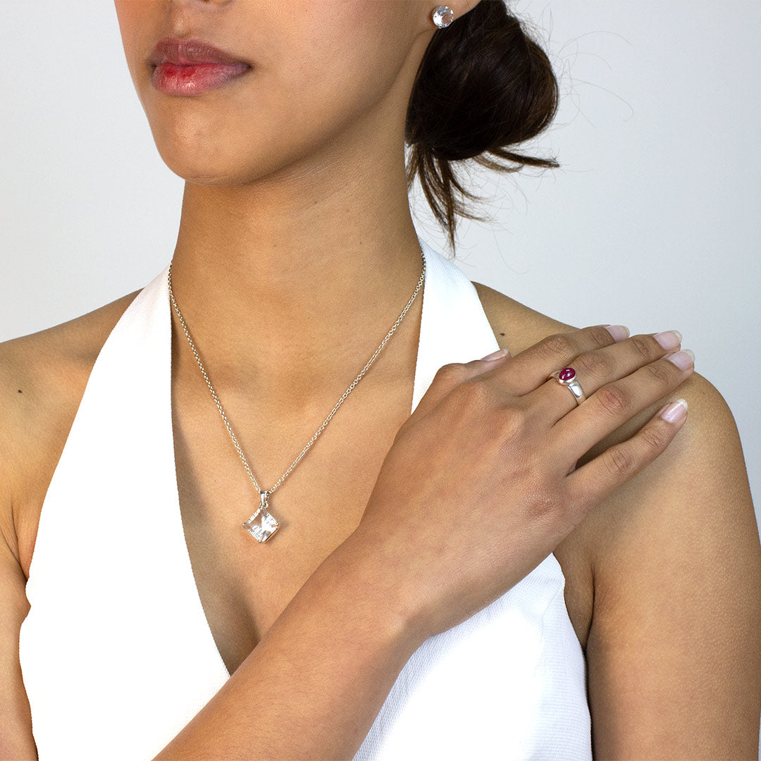 Woman wearing a silver ring with a red gemstone on a plain background