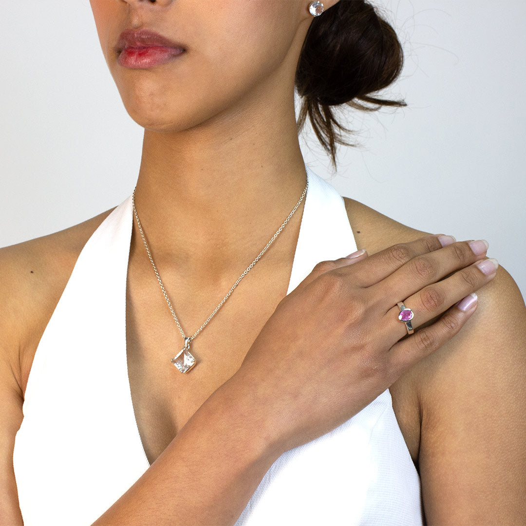 Woman wearing a silver ring with a pink gemstone on a plain background