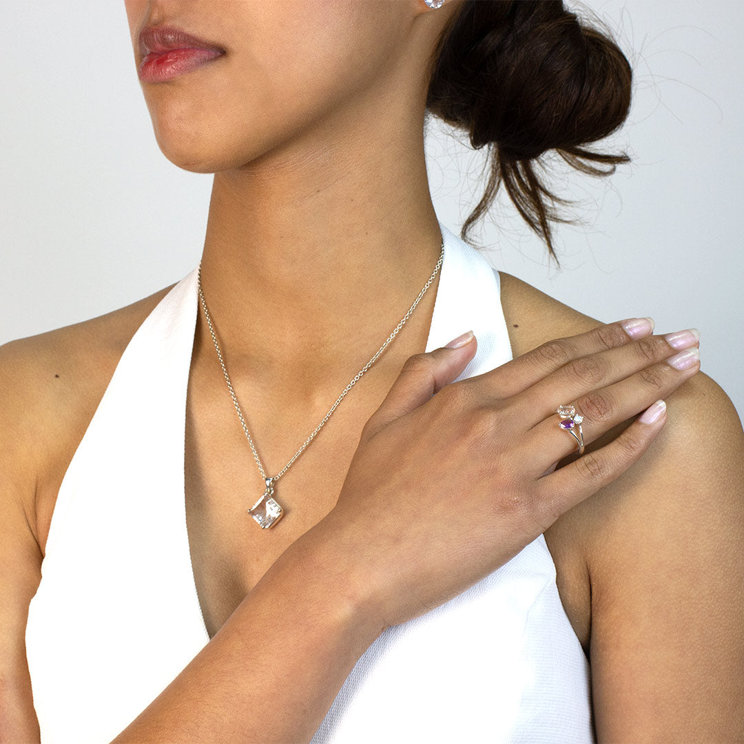 Woman wearing a silver ring with purple and clear gemstones on a plain background