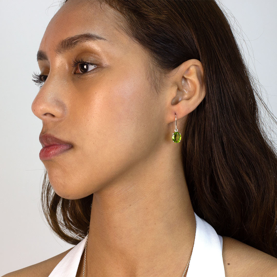 Woman wearing a silver drop earring with green gemstone on a plain background