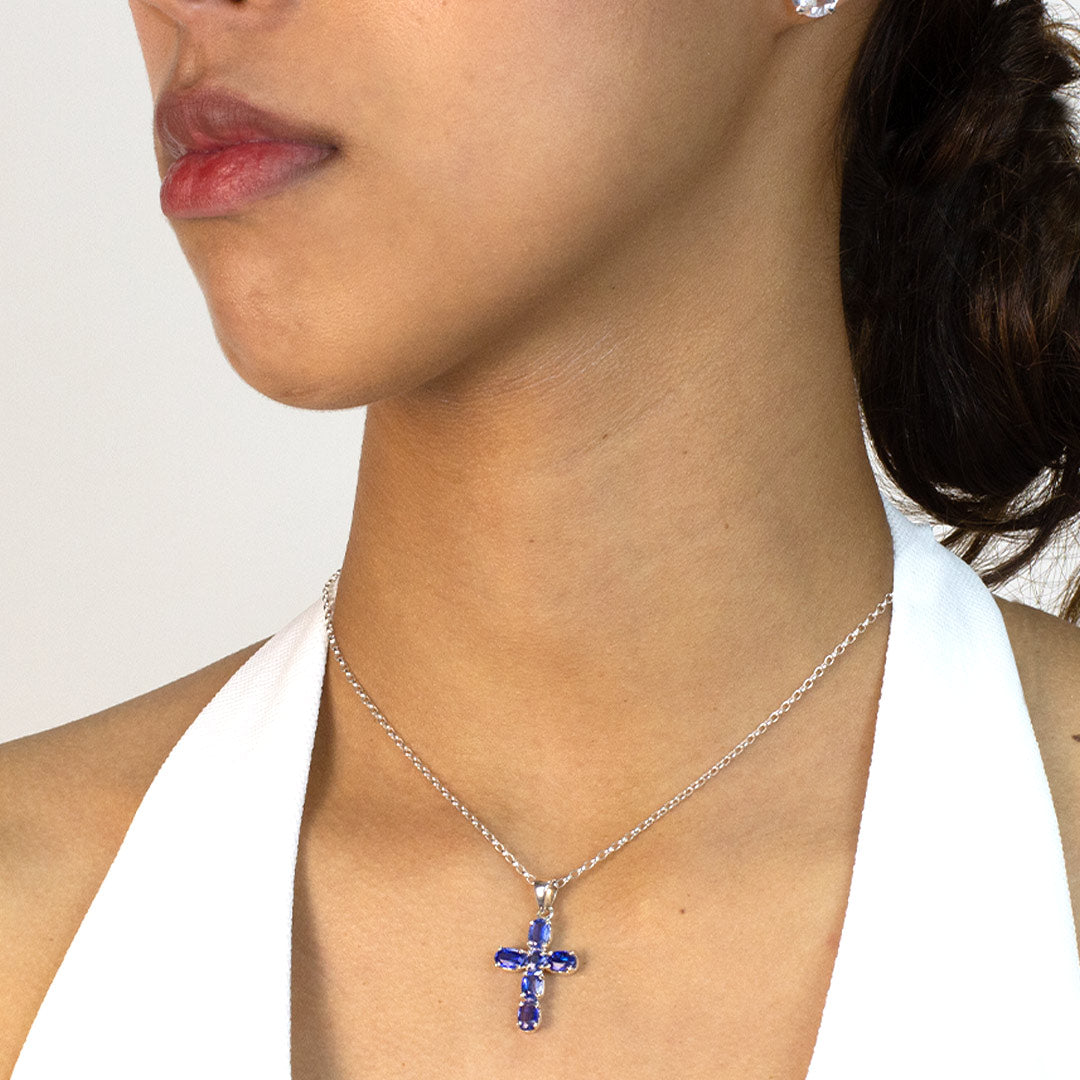 Woman wearing a silver cross pendant with blue gemstones on a plain background