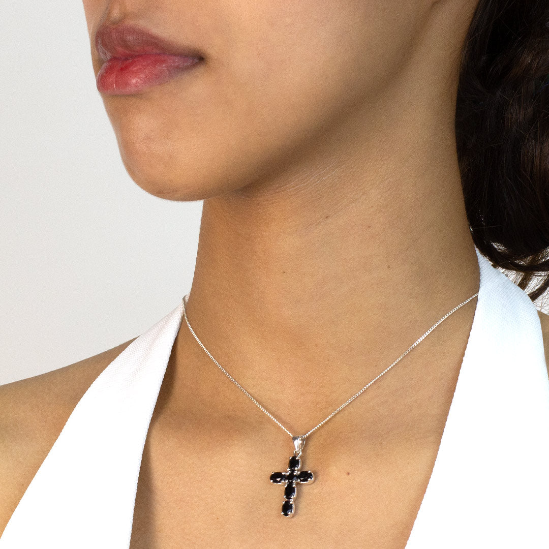 Woman wearing a black cross pendant necklace on a plain background