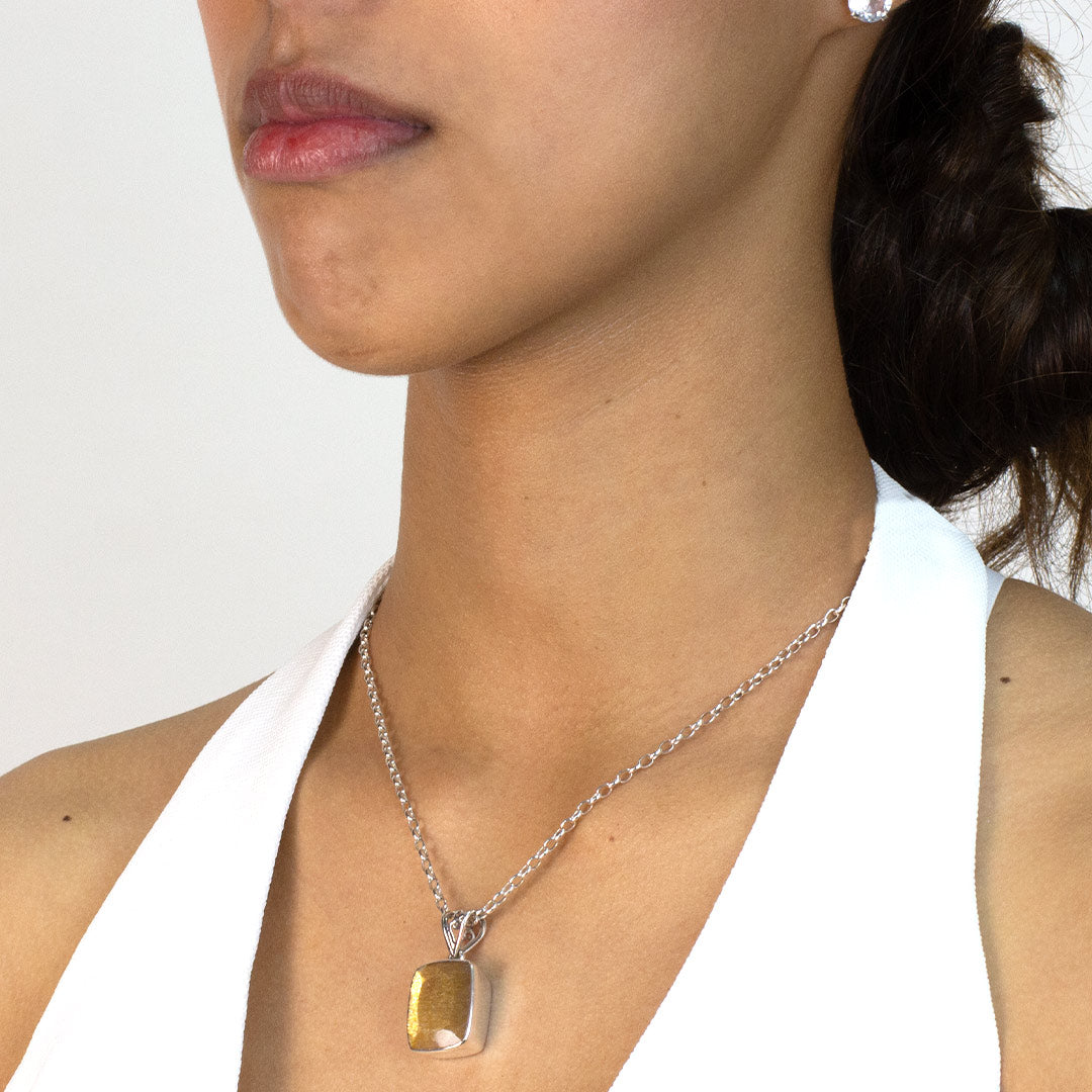 Woman wearing a golden pendant on a silver chain against a plain background