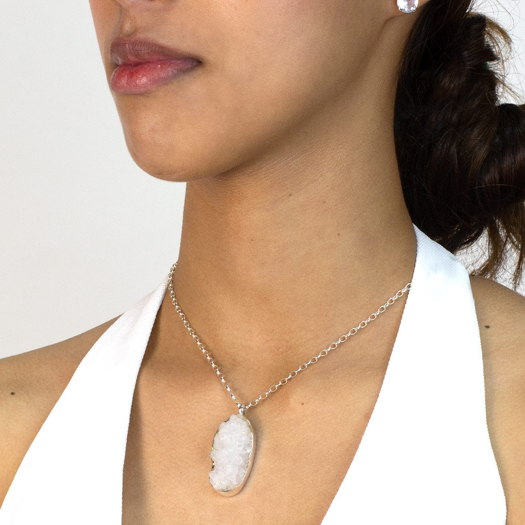 Woman wearing a silver necklace with an oval-shaped druzy stone pendant on a plain background