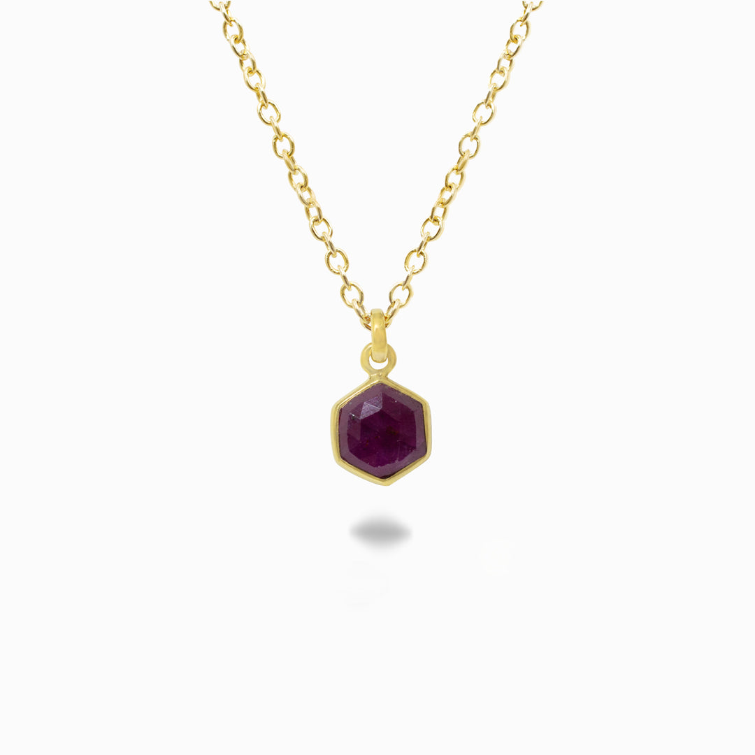Gold necklace with a dark pink gemstone pendant on a white background