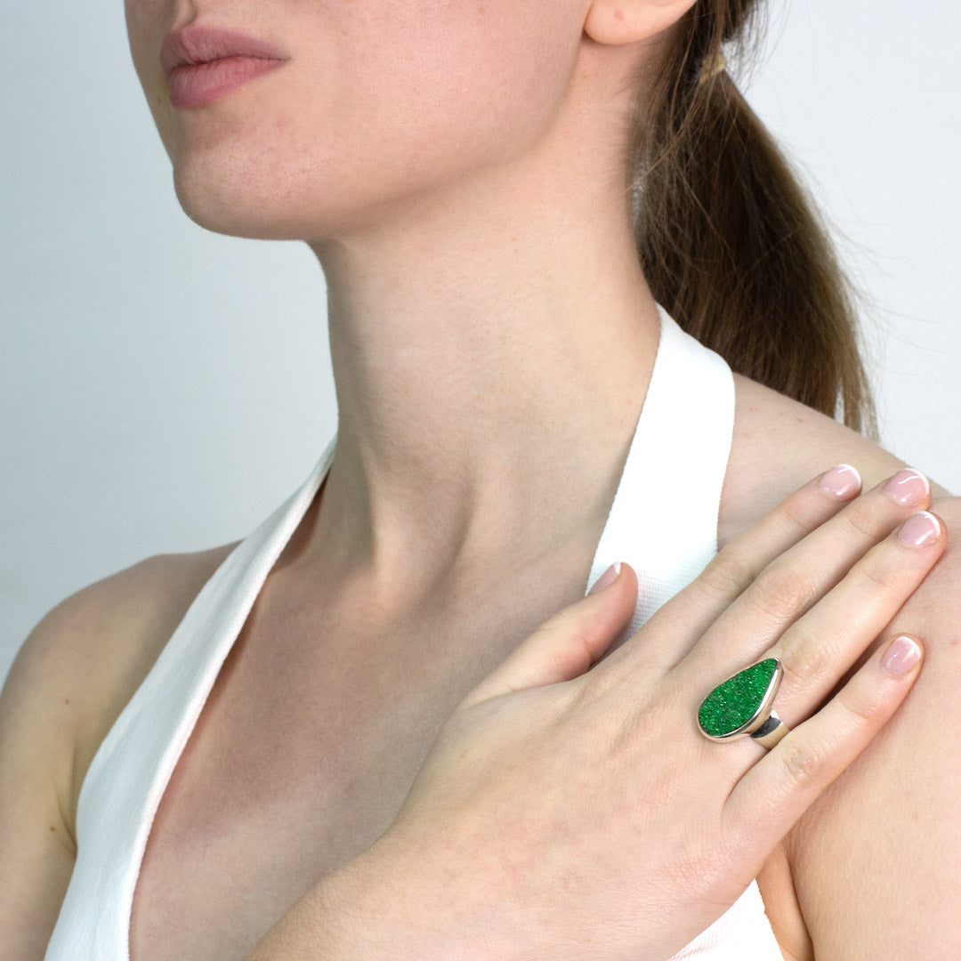 Woman wearing a silver ring with a green stone on a plain background